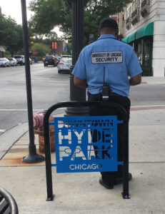 University of Chicago security leaning against "Downtown Hyde Park Chicago" sign